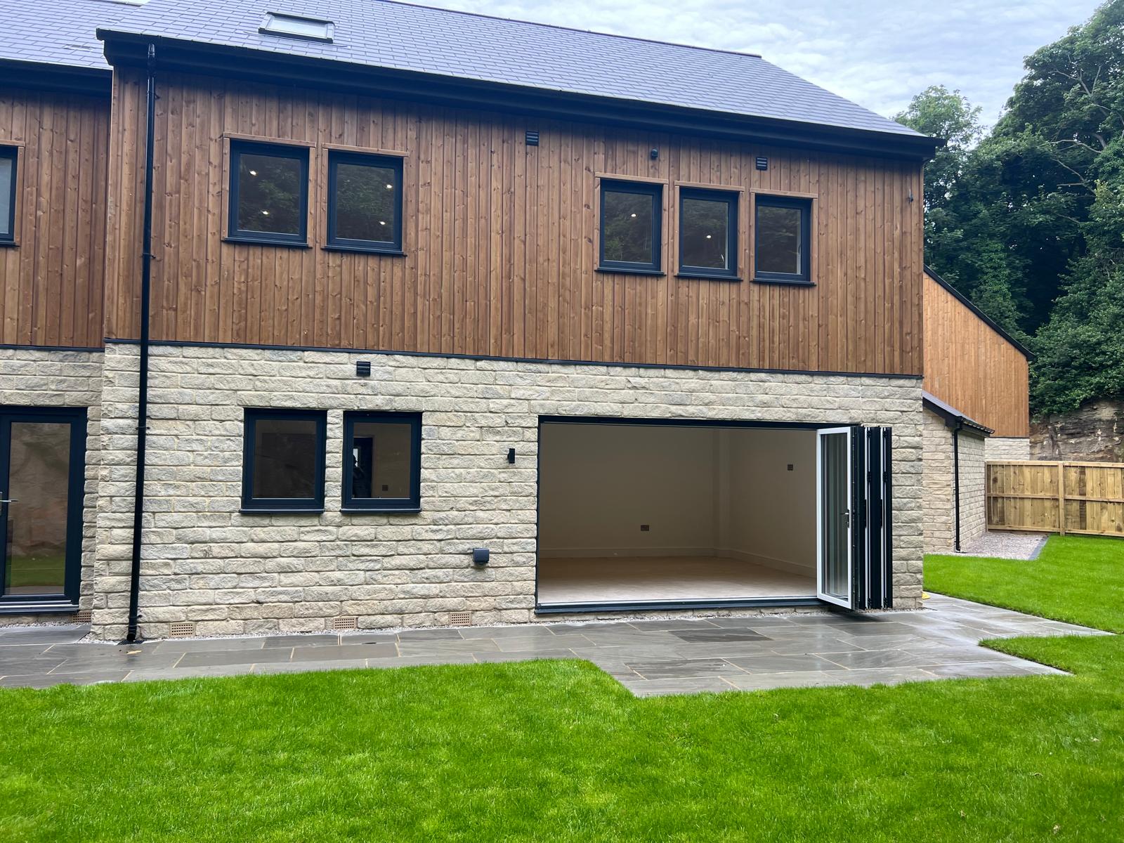Stone and timber-clad extension with anthracite grey aluminium bifold doors and matching windows
