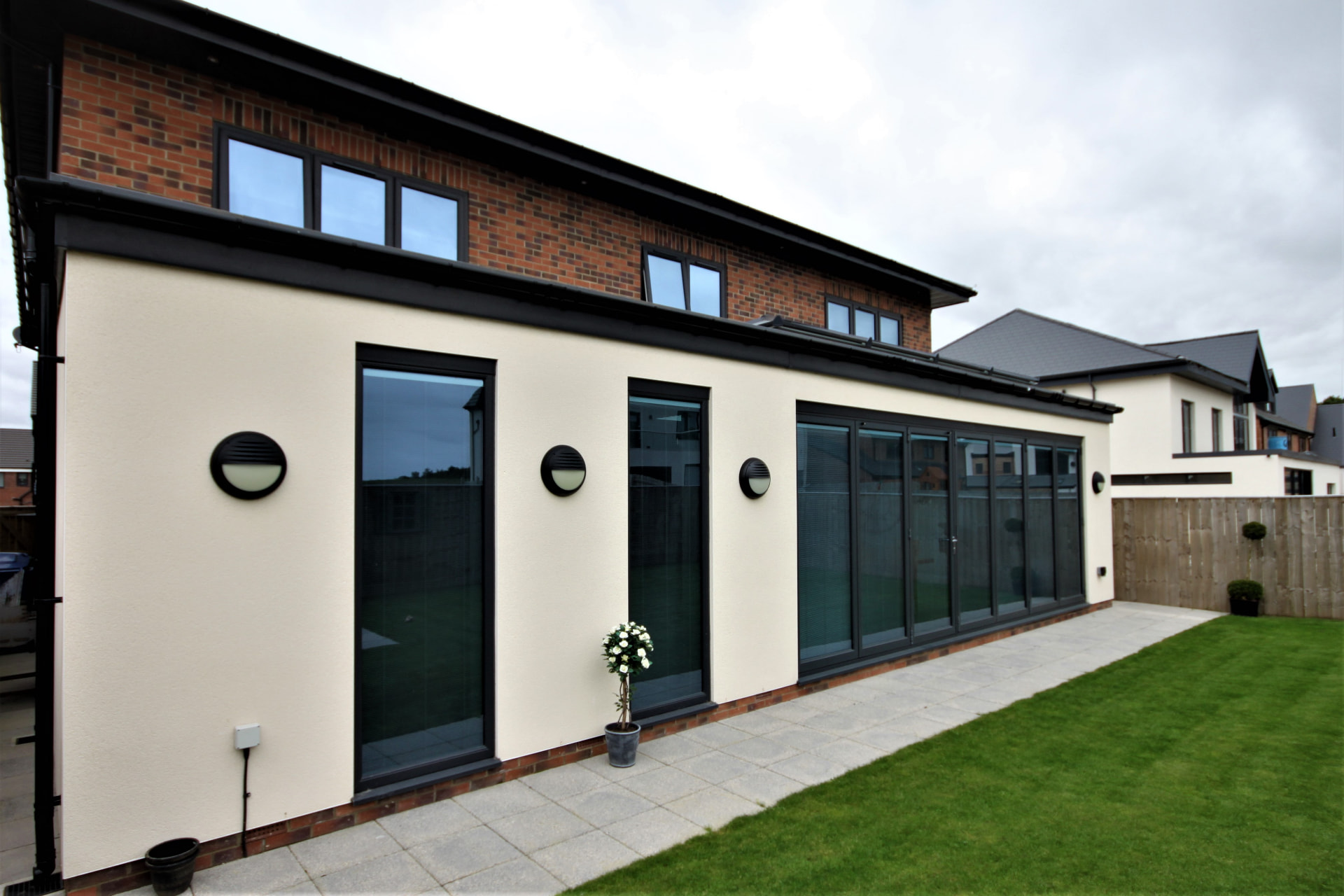 Long run of anthracite grey aluminium bifold doors on a modern white rendered extension