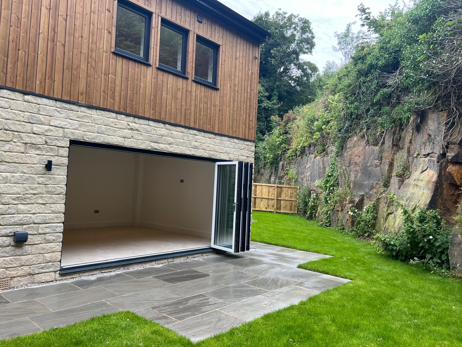 Side elevation of a stone and timber extension with anthracite grey bifold doors open