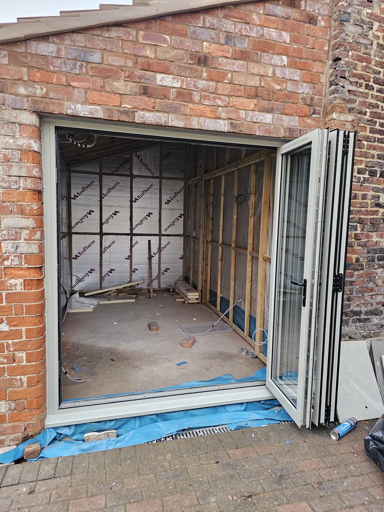 Three-panel pebble grey bifold doors folded and stacked within a brick aperture