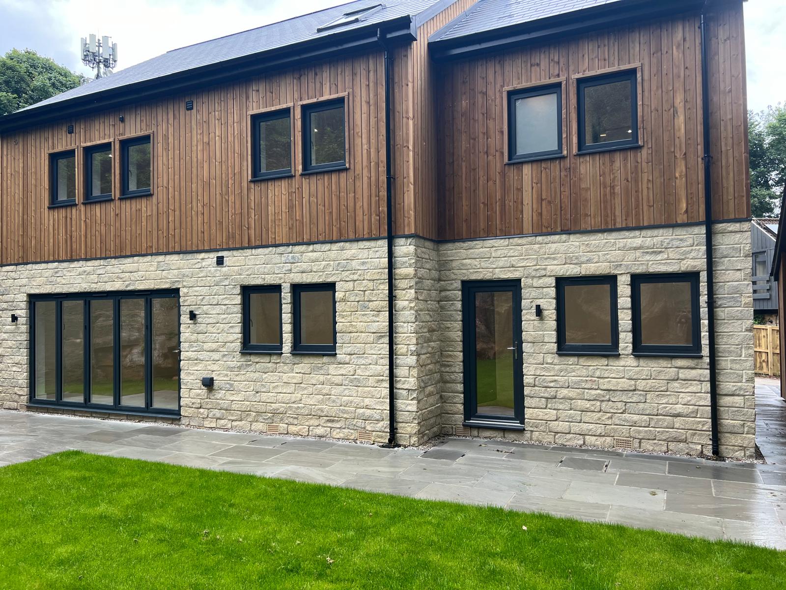 Rear elevation of a stone and timber extension with anthracite grey bifold doors, door and windows