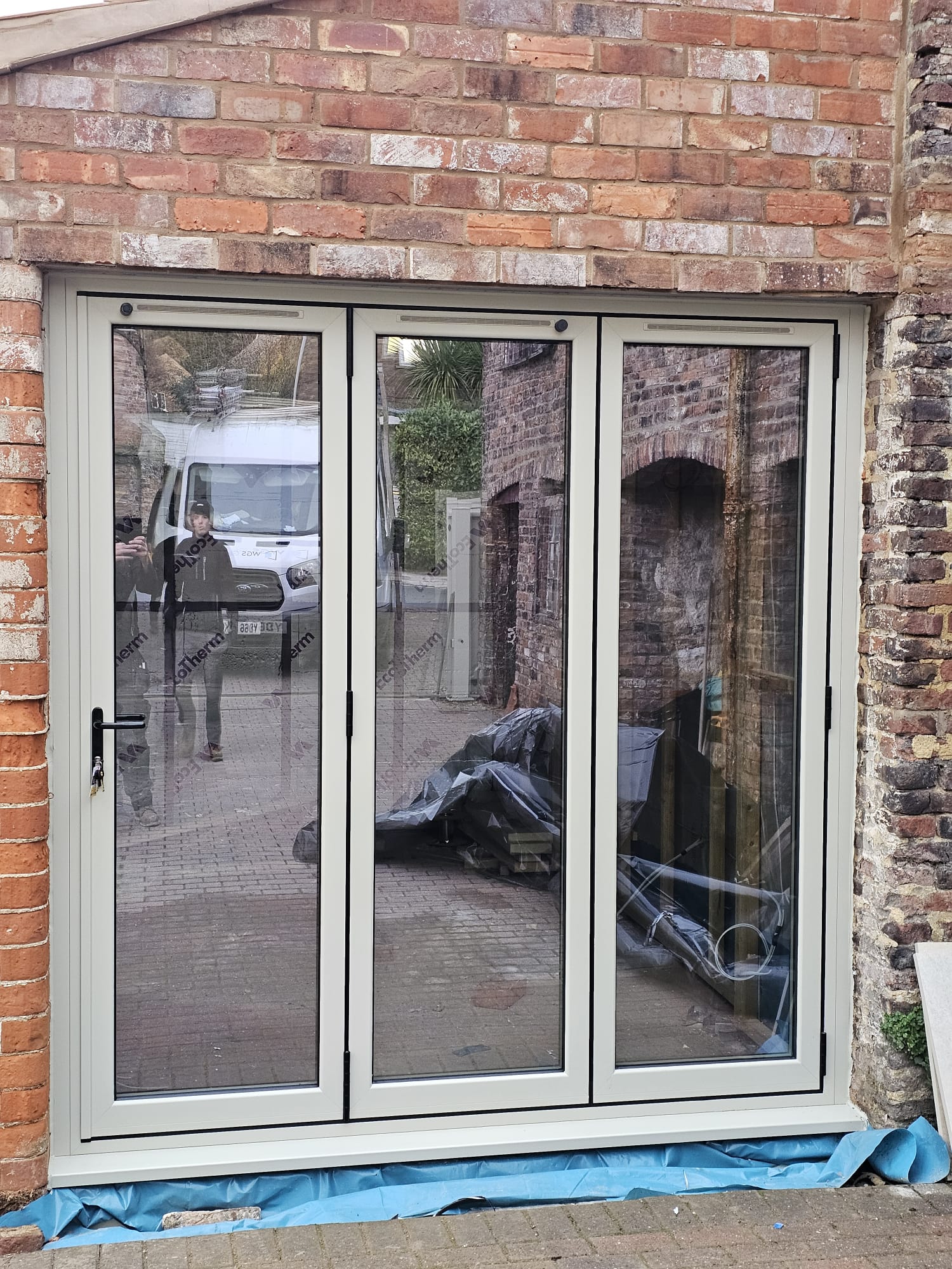 Three-panel pebble grey aluminium bifold doors installed in a brick opening