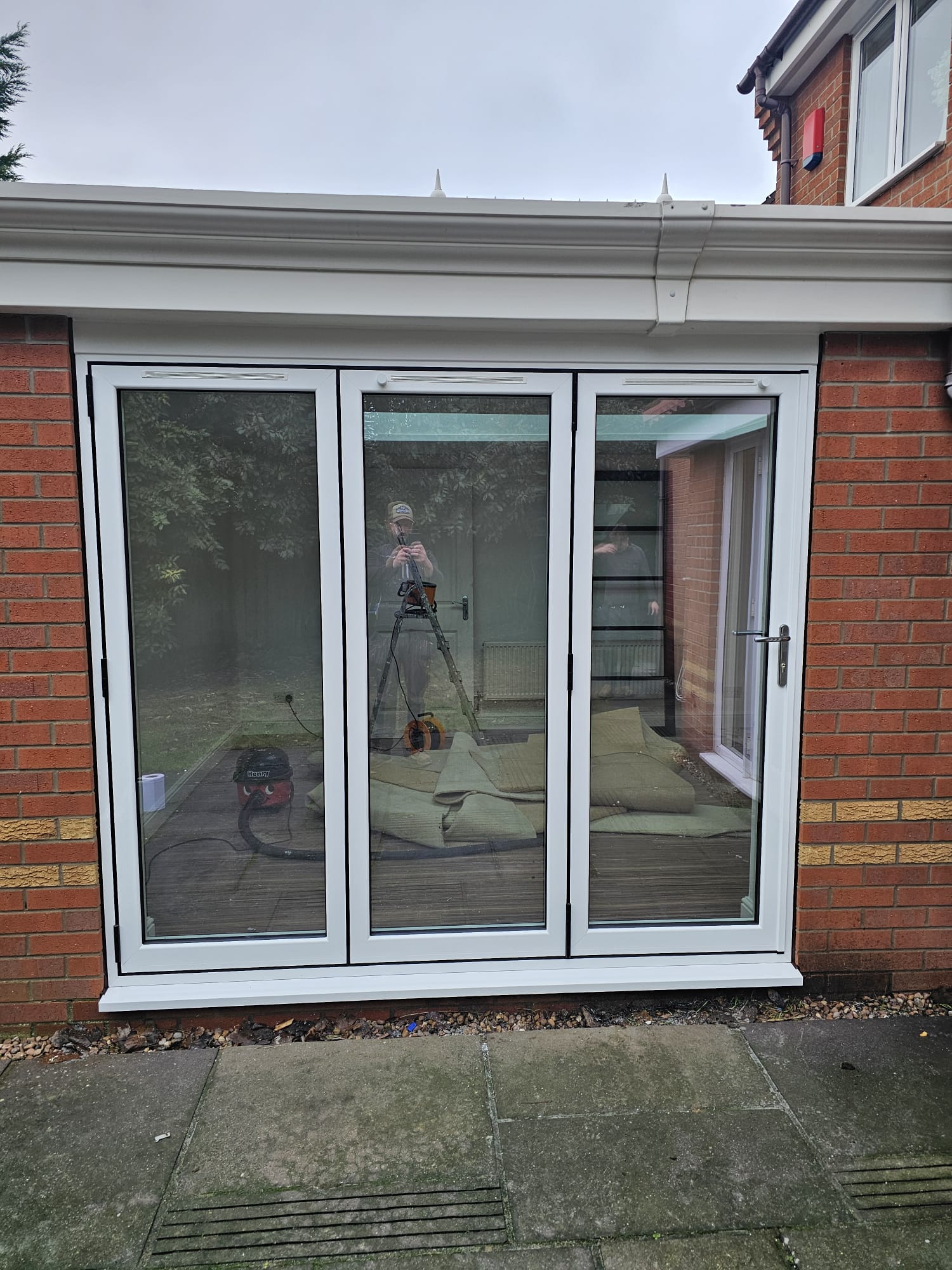 Three-panel white aluminium bifold doors closed, seen from outside a brick home