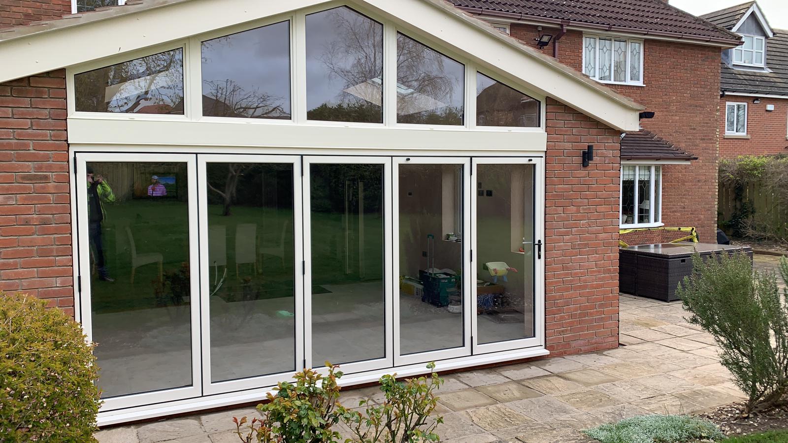 Five-panel cream aluminium bifold doors with a shaped glazed frame above on a brick extension
